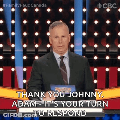A Man In A Suit And Tie Is Standing On A Stage And Says Thank You Johnny Adam It 'S Your Turn To Respond GIF