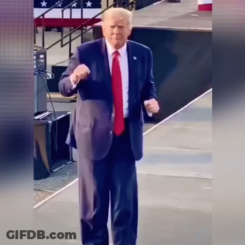 A Man In A Suit And Tie Is Standing On A Stage Giving A Fist Bump GIF