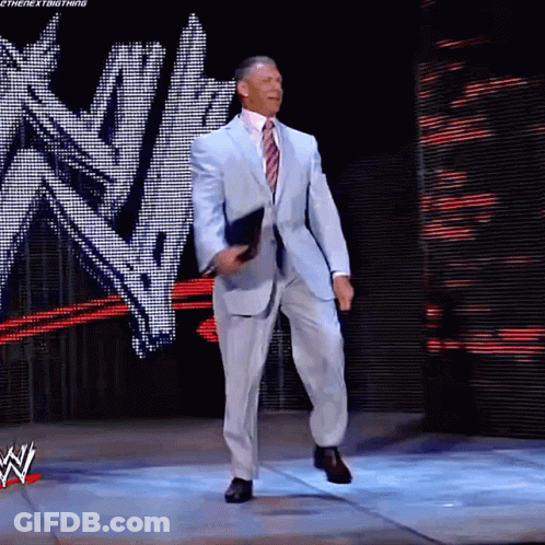 A Man In A Suit And Tie Is Standing On A Stage In Front Of A Wwe Logo GIF