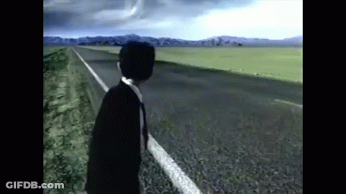 A Man In A Suit And Tie Is Standing On The Side Of A Highway . GIF