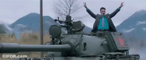 A Man In A Suit And Tie Is Standing On Top Of A Tank With His Arms In The Air GIF