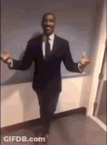 A Man In A Suit And Tie Is Standing With His Arms Outstretched In A Hallway . GIF