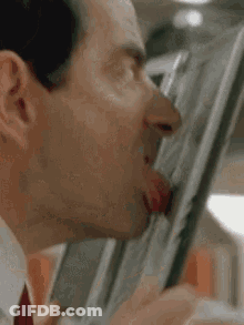 A Man In A Suit And Tie Is Sticking His Tongue Out While Eating Something . GIF