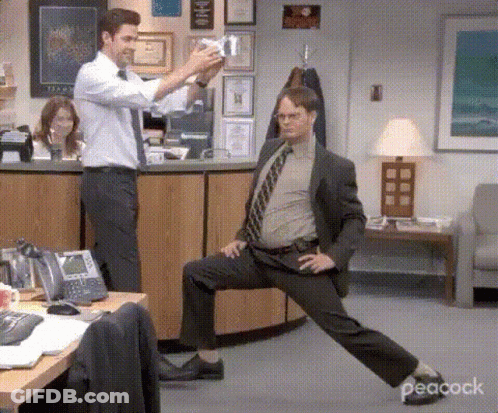 A Man In A Suit And Tie Is Stretching His Legs In An Office While Another Man Takes A Picture Of Him . GIF