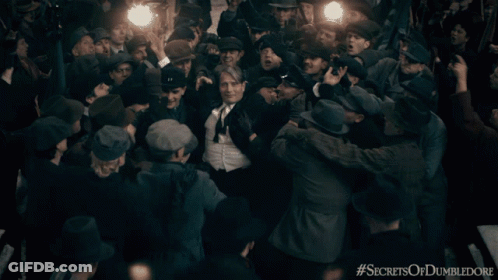 A Man In A Suit And Tie Is Surrounded By A Crowd With The Hashtag Secrets Of Dumbledore On The Bottom GIF