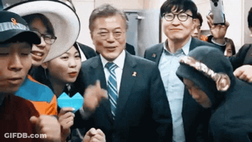 A Man In A Suit And Tie Is Surrounded By A Group Of People . GIF