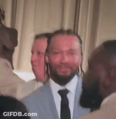 A Man In A Suit And Tie Is Surrounded By Other People GIF