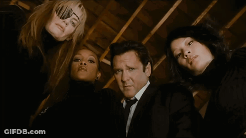 A Man In A Suit And Tie Is Surrounded By Three Women In Black GIF