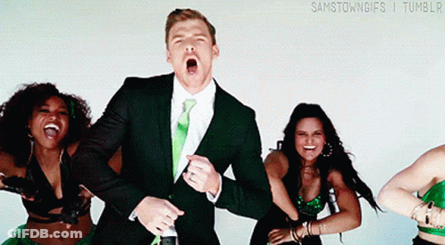 A Man In A Suit And Tie Is Surrounded By Women In Green Outfits GIF