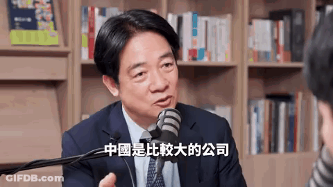 A Man In A Suit And Tie Is Talking Into A Microphone In Front Of A Bookshelf In A Library . GIF