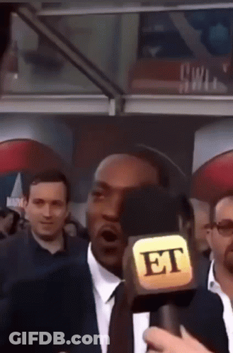 A Man In A Suit And Tie Is Talking Into A Microphone That Says Et GIF