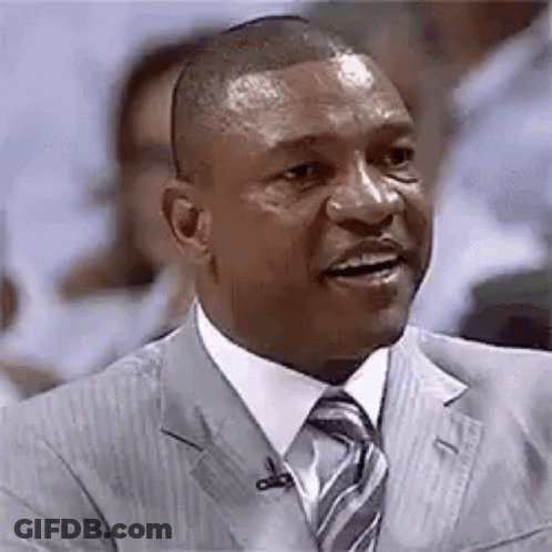 A Man In A Suit And Tie Is Talking Into A Microphone While Sitting In Front Of A Crowd . GIF