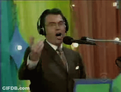 A Man In A Suit And Tie Is Talking Into A Microphone With Headphones On . GIF