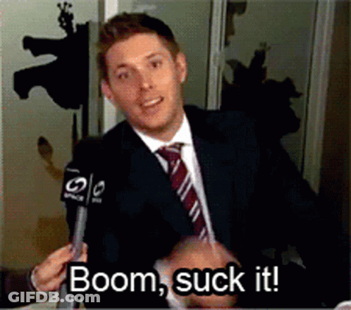 A Man In A Suit And Tie Is Talking Into A Microphone With The Words Boom Suck It Below Him GIF