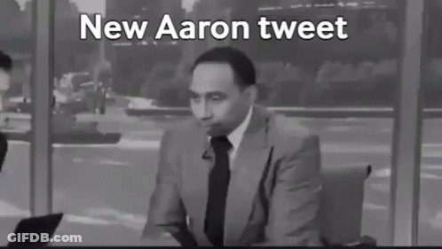 A Man In A Suit And Tie Is Talking Into A Microphone With The Words New Aaron Tweet Below Him . GIF