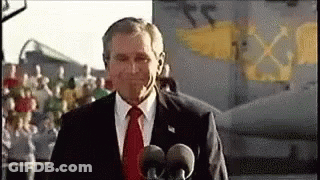 A Man In A Suit And Tie Is Talking Into Two Microphones . GIF