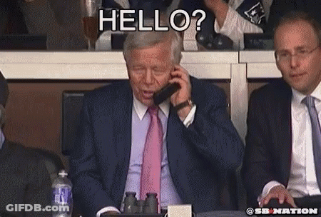 A Man In A Suit And Tie Is Talking On A Cell Phone While Another Man Says Hello GIF