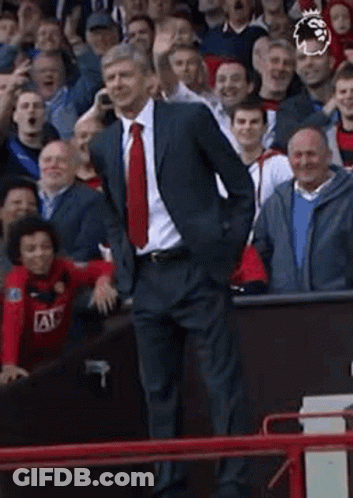 A Man In A Suit And Tie Is Talking On A Cell Phone While Standing In Front Of A Crowd Of People . GIF