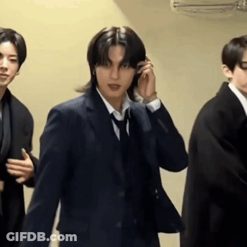 A Man In A Suit And Tie Is Talking On A Cell Phone While Standing Next To Two Other Men In Suits . GIF