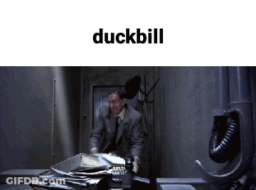 A Man In A Suit And Tie Is Talking On A Phone In A Dark Room With The Word Duckbill Above Him GIF