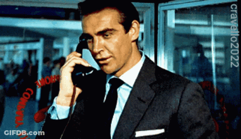 A Man In A Suit And Tie Is Talking On A Phone In Front Of A Sign That Says Chrome GIF