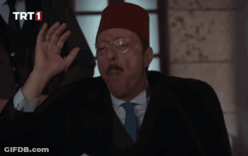 A Man In A Suit And Tie Is Talking On A Phone With A Trt1 Logo In The Corner GIF