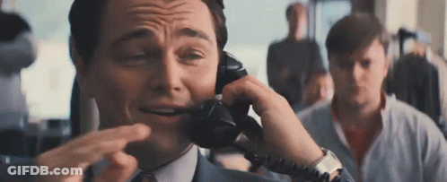 A Man In A Suit And Tie Is Talking On A Telephone While Making A Funny Face . GIF