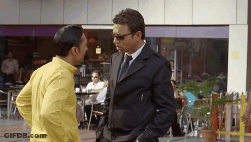 A Man In A Suit And Tie Is Talking To A Man In A Yellow Shirt GIF