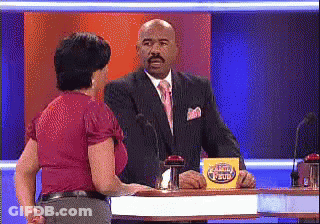 A Man In A Suit And Tie Is Talking To A Woman In A Red Shirt On A Game Show GIF