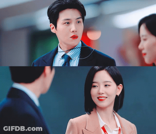 A Man In A Suit And Tie Is Talking To A Woman In A Tan Jacket GIF