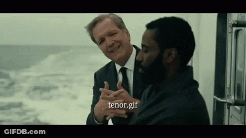 A Man In A Suit And Tie Is Talking To Another Man In A Black Shirt . GIF