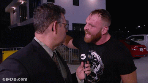 A Man In A Suit And Tie Is Talking To Another Man In A Black Shirt That Says Tnt GIF
