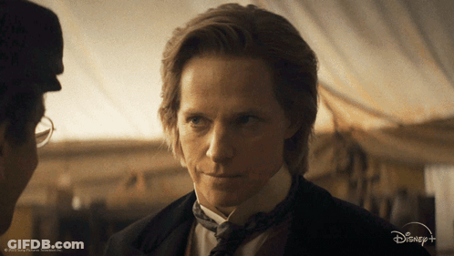 A Man In A Suit And Tie Is Talking To Another Man In A Disney + Advertisement GIF