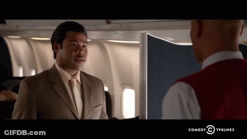 A Man In A Suit And Tie Is Talking To Another Man In A Red Vest Which Says Comedy Central GIF
