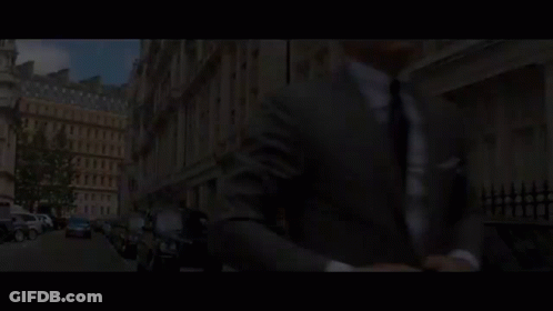 A Man In A Suit And Tie Is Talking To Another Man In A Room With A Sign In A Foreign Language GIF