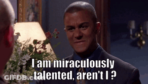 A Man In A Suit And Tie Is Talking To Another Man In Front Of A Lamp And Flowers . GIF