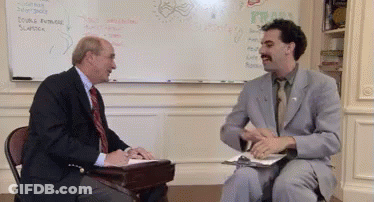 A Man In A Suit And Tie Is Talking To Another Man In Front Of A White Board GIF