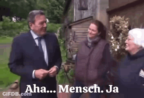 A Man In A Suit And Tie Is Talking To Two Women In Front Of A Building With The Words Aha Mensch Ja On The Bottom GIF