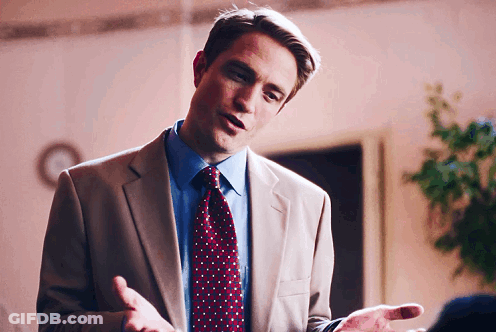 A Man In A Suit And Tie Is Talking With His Hands Outstretched GIF