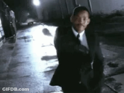 A Man In A Suit And Tie Is Walking Down A Dark Street At Night . GIF