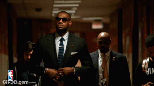 A Man In A Suit And Tie Is Walking Down A Hallway GIF