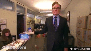 A Man In A Suit And Tie Is Walking Down A Hallway With Makeagif.com Written On The Bottom GIF
