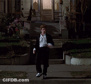 A Man In A Suit And Tie Is Walking Down A Street At Night GIF