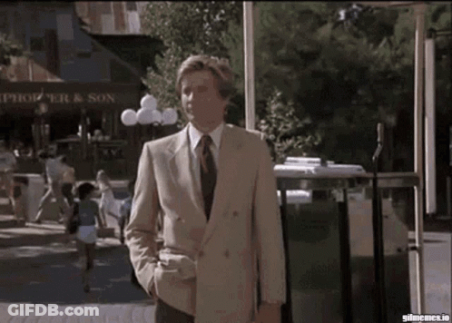 A Man In A Suit And Tie Is Walking Down A Street In Front Of A Store That Says Springer & Son GIF