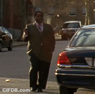 A Man In A Suit And Tie Is Walking Down A Street GIF