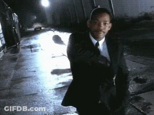 A Man In A Suit And Tie Is Walking Down A Wet Sidewalk GIF