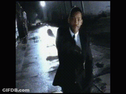 A Man In A Suit And Tie Is Walking Down A Wet Street GIF