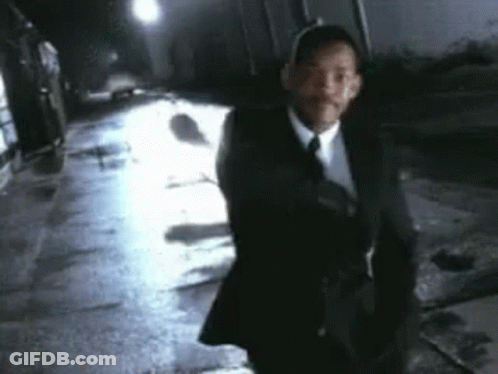 A Man In A Suit And Tie Is Walking Down A Wet Street At Night . GIF