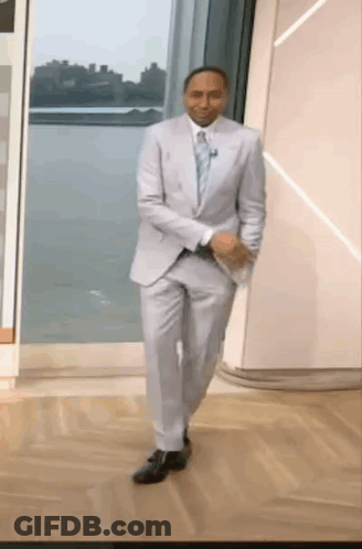 A Man In A Suit And Tie Is Walking Down A Wooden Floor . GIF