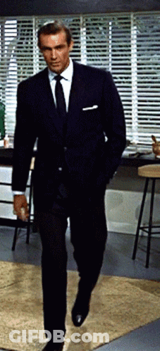 A Man In A Suit And Tie Is Walking In A Kitchen GIF